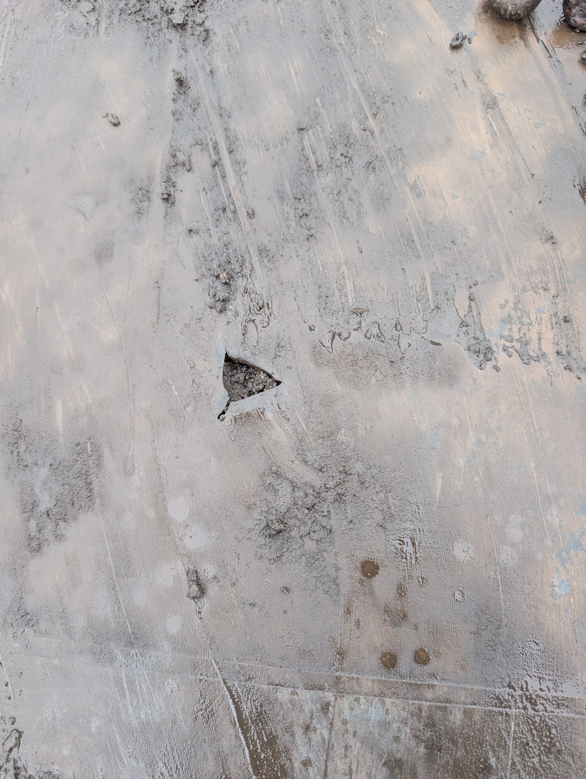 Overhead view of a rough, light-colored surface with a dark, triangular shape in the center.