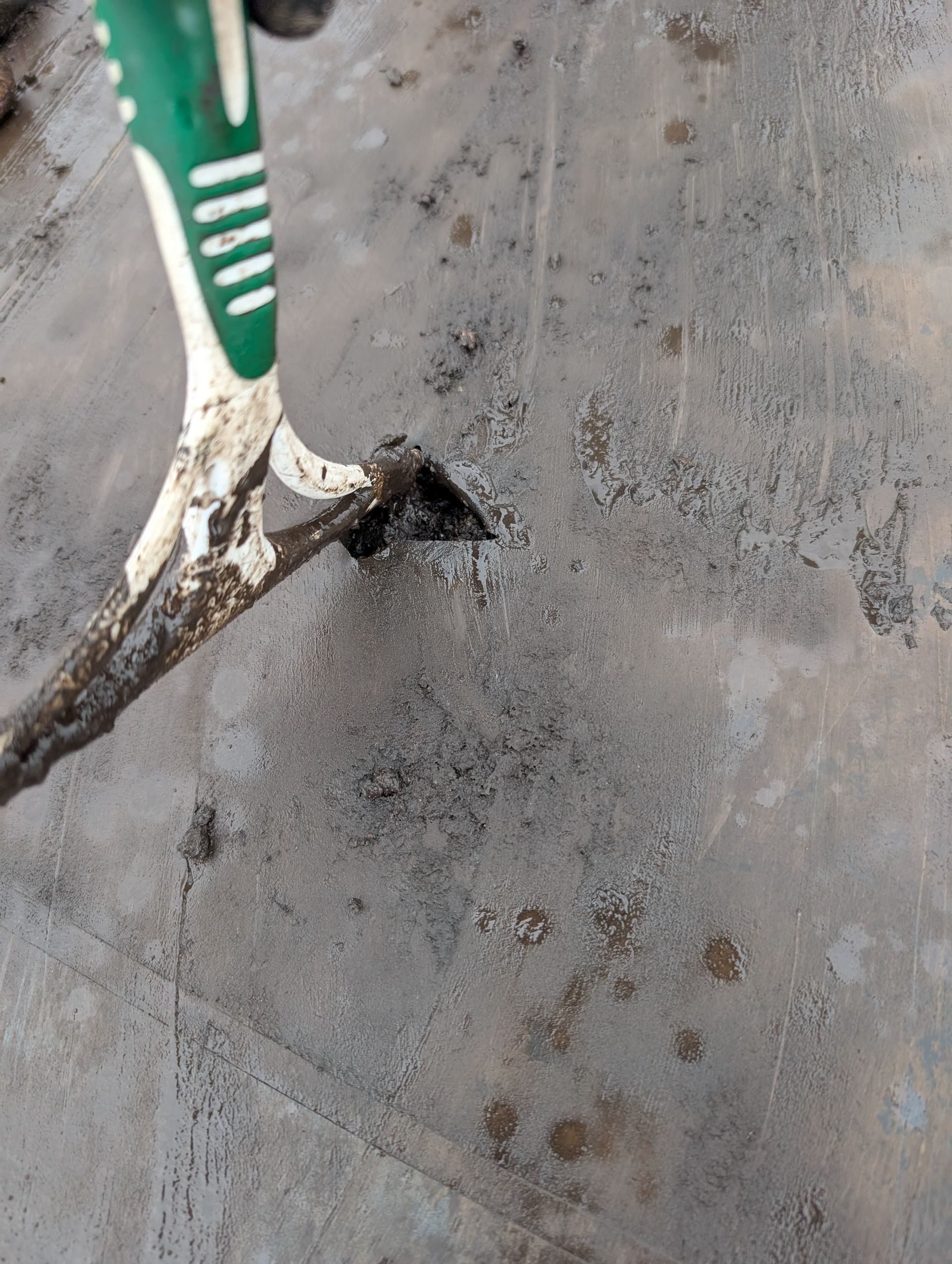 Scraper removing a dark substance from a grey surface. Green and white handle visible.