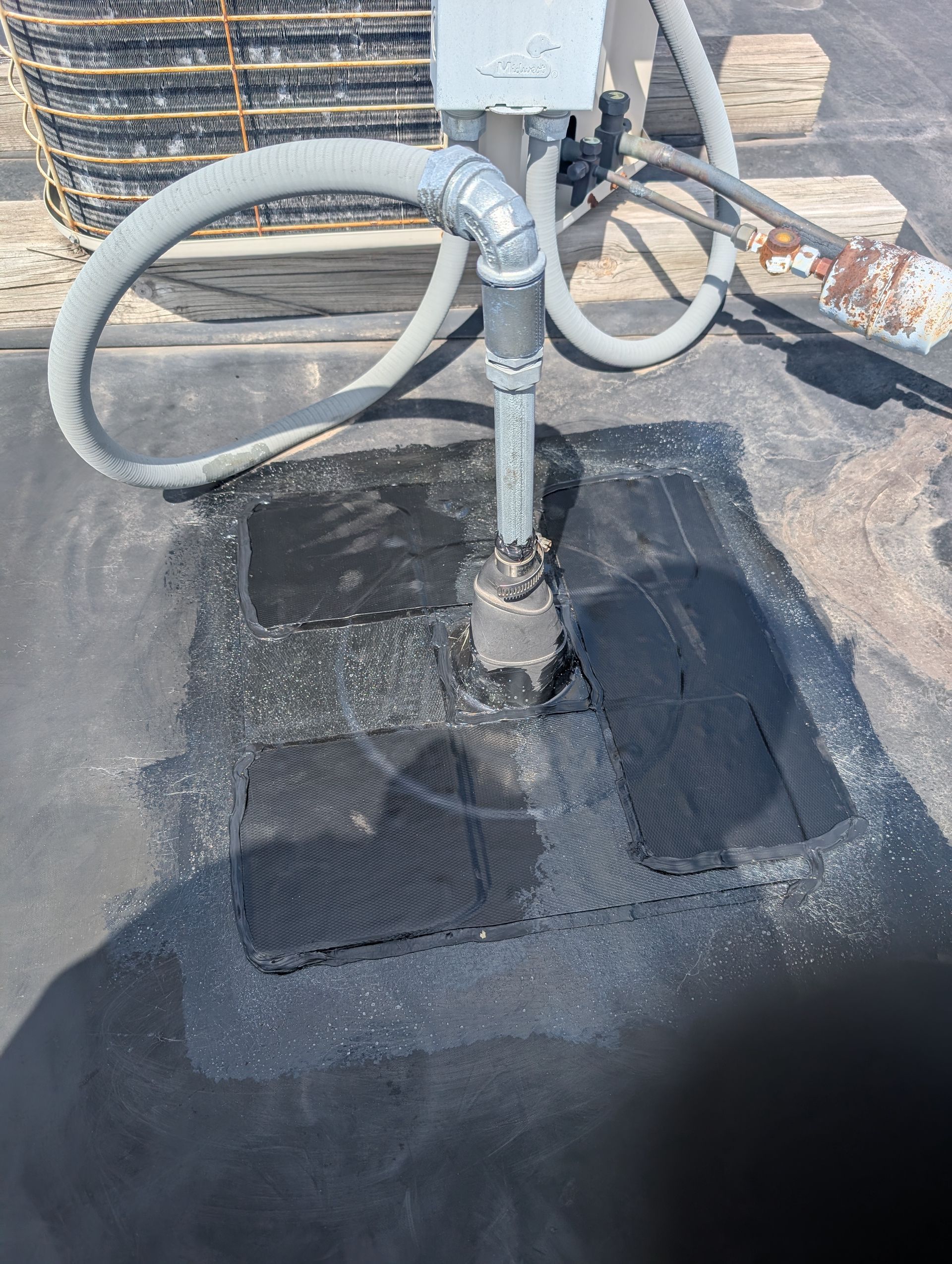 Black roof with patched areas and plumbing fixture.