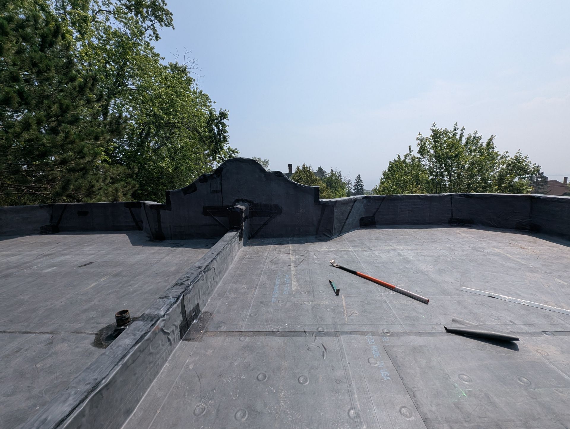 Flat roof with a central raised structure, surrounded by trees under a blue sky.