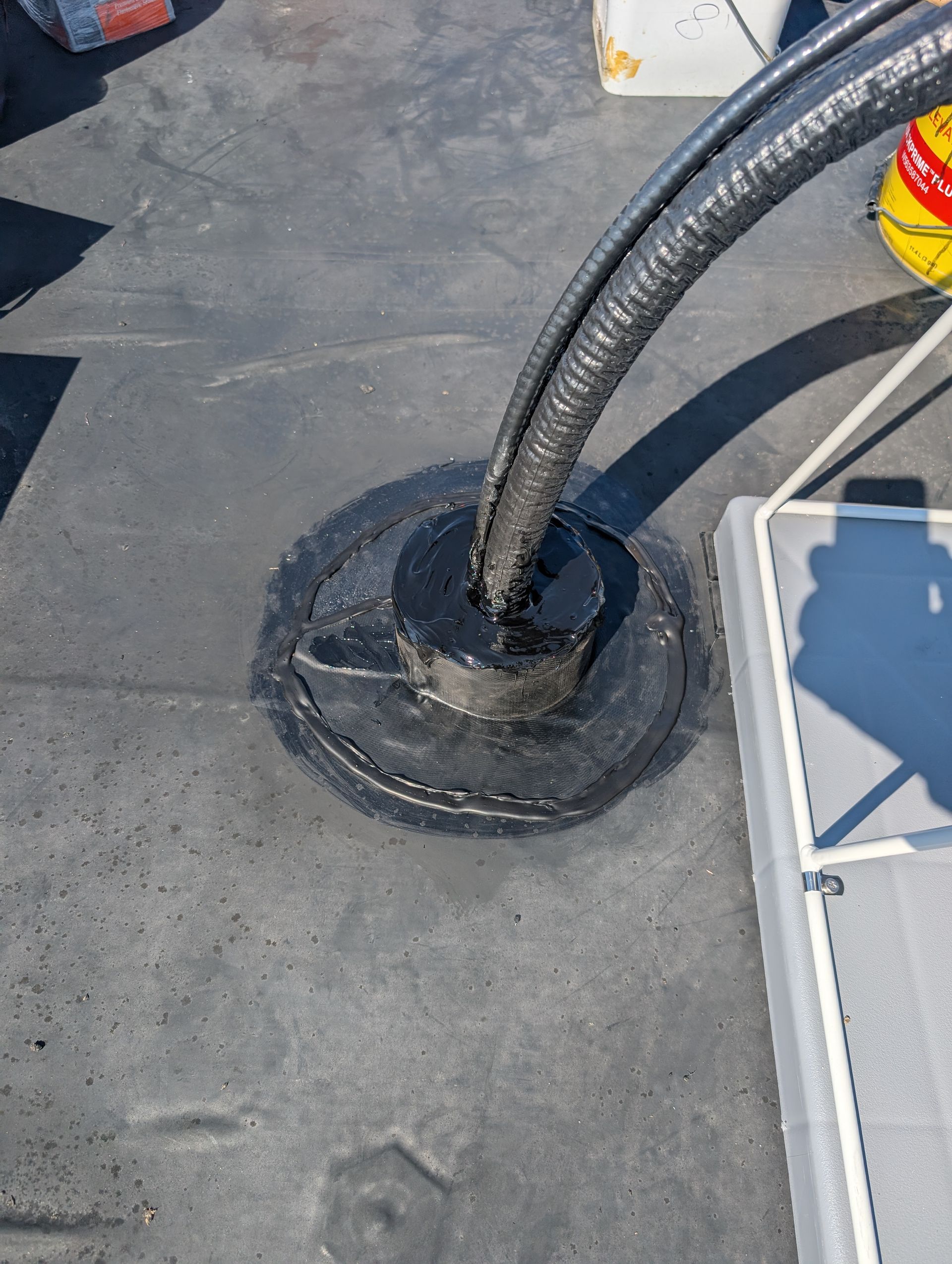 Black tube exiting a roof, sealed with black sealant around the base.