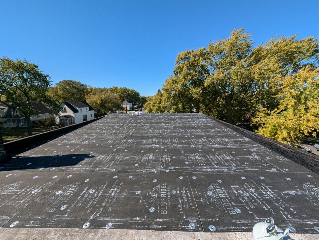 Black flat roof with many white fasteners, under a bright blue sky.