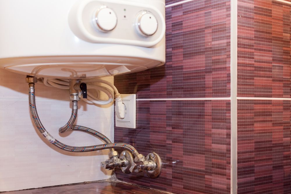 White Water Heater on a Textured Red-Brown Tile Wall Connected on Outlet — Illawater Hot Water Services in Wollongong, NSW