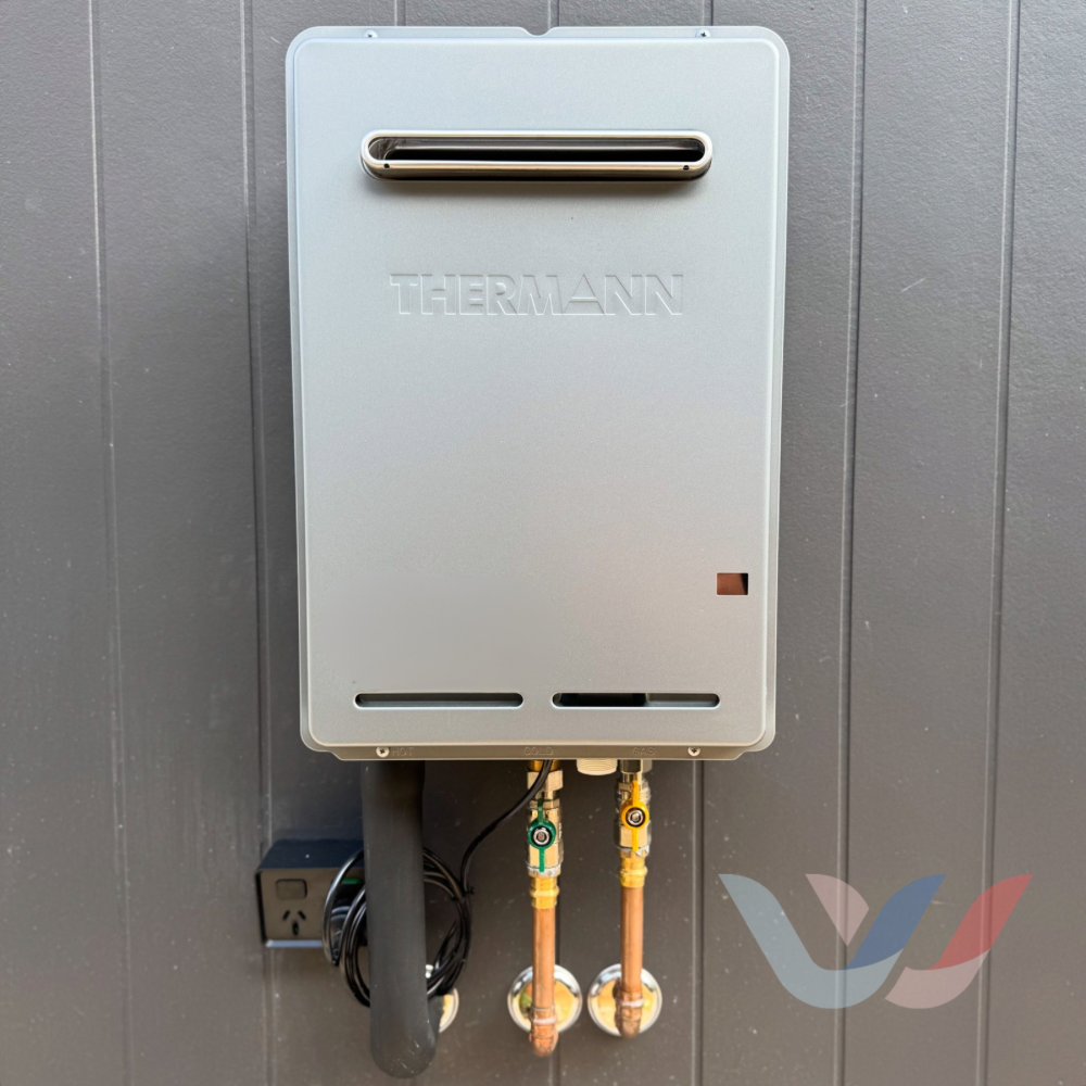 Gray Thermann tankless water heater mounted on a gray wall. Copper pipes and black cable visible. — Illawater Hot Water Services in East Corrimal, NSW