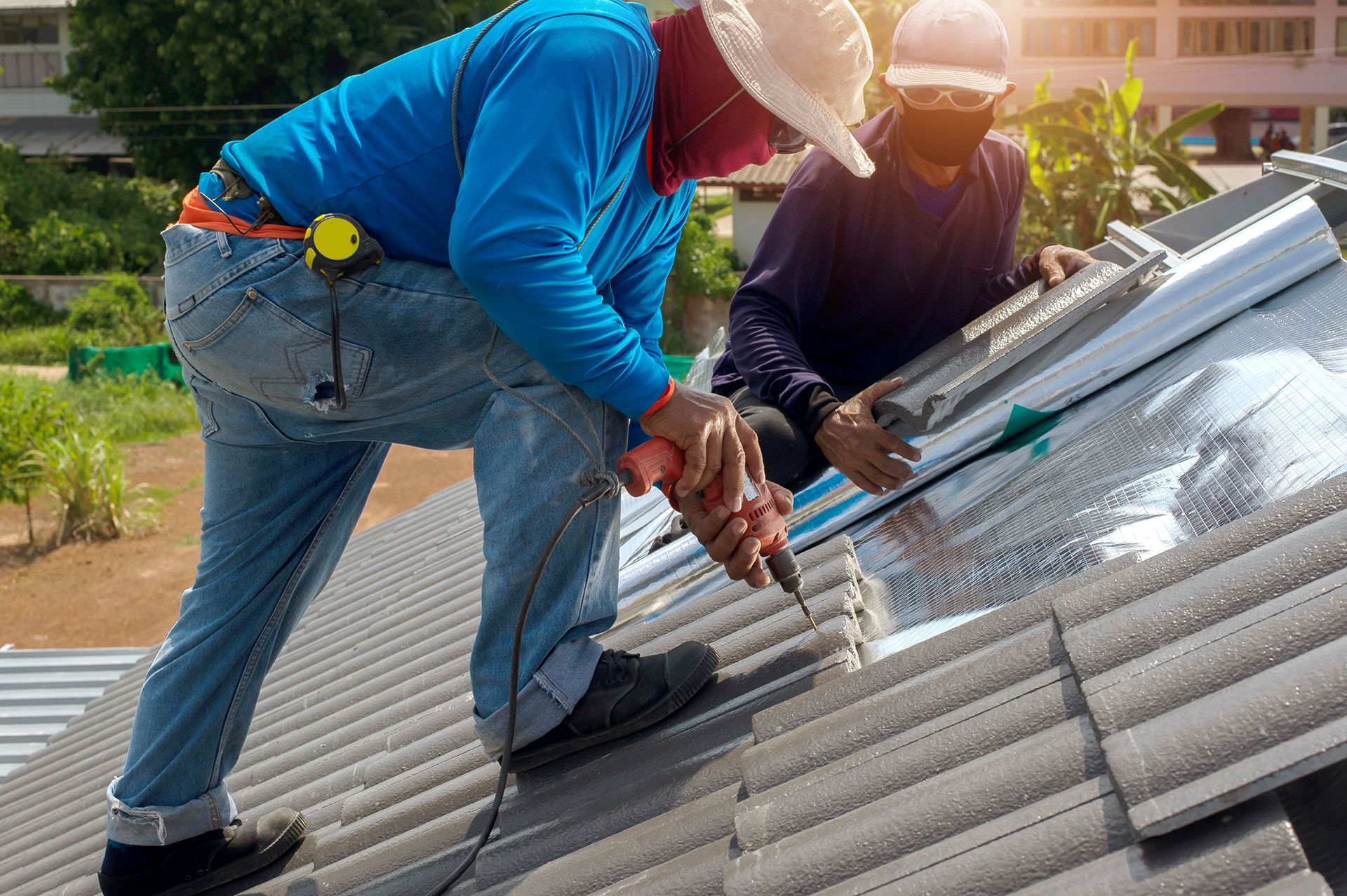 Two men are working on a roof with a drill.