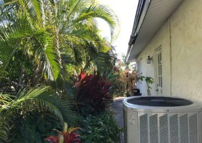 A large air conditioner is sitting on the side of a house surrounded by trees.