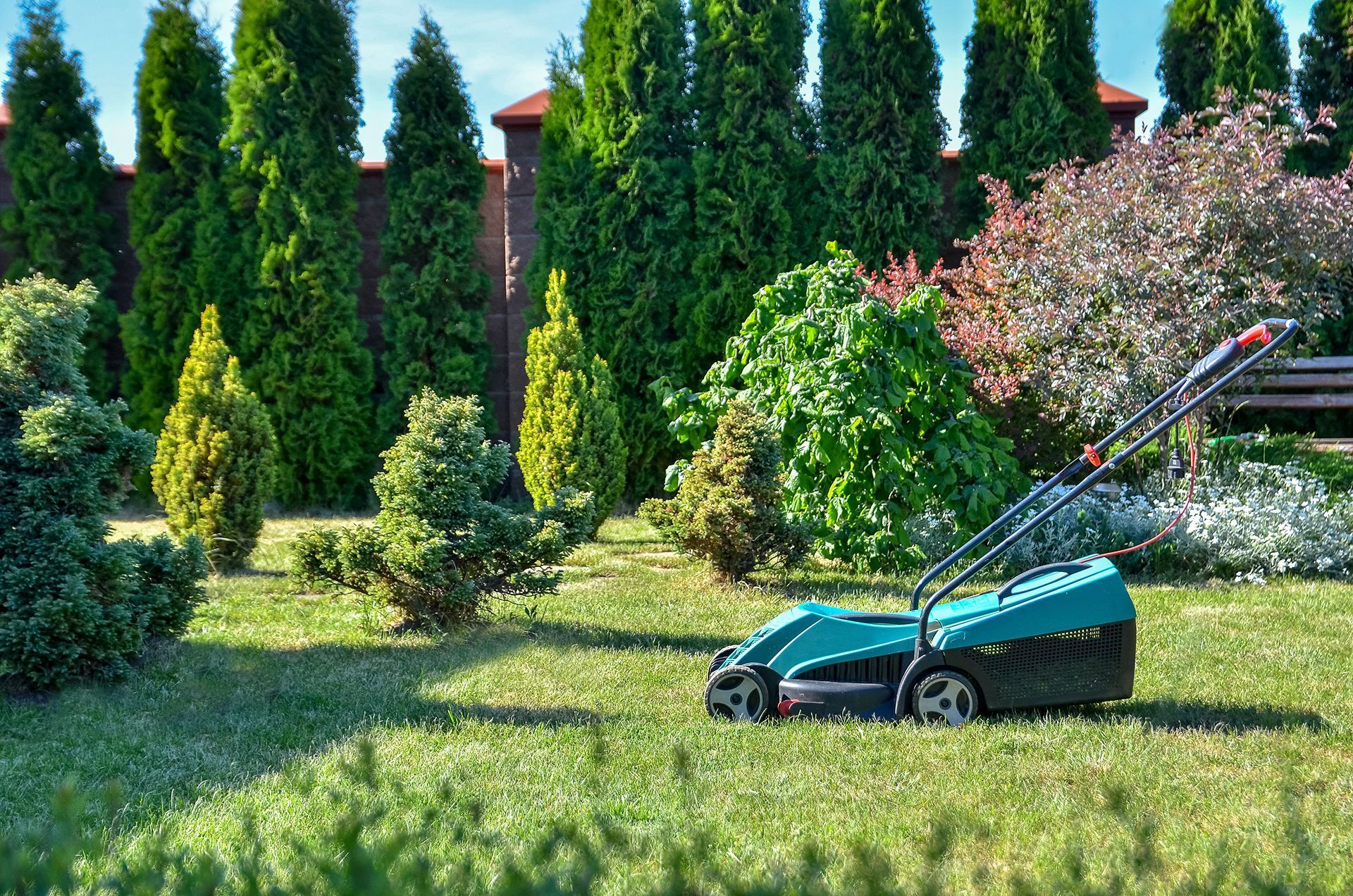 A person is using a lawn mower to cut the grass in a garden.
