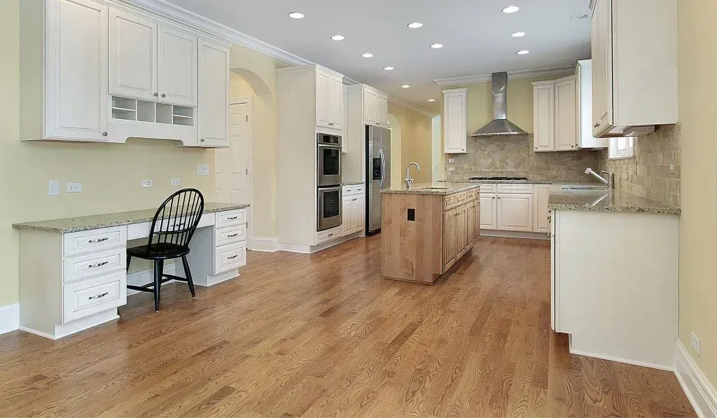 An empty kitchen with hardwood floors and white cabinets
