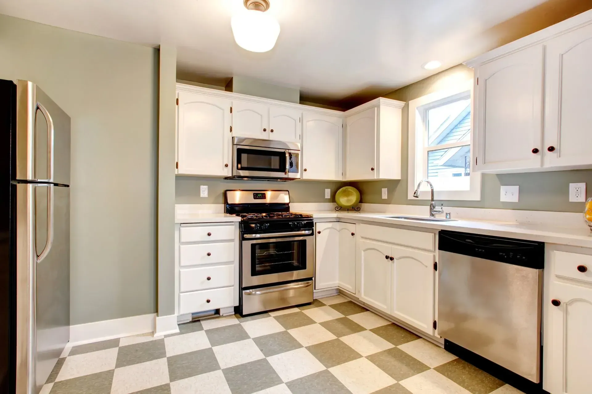 A kitchen with white cabinets, stainless steel appliances, and a checkered floor