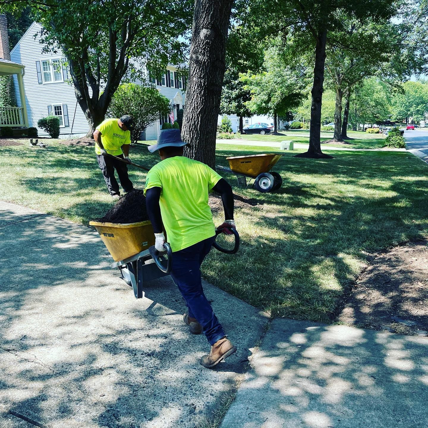 Person in a straw hat and green shirt gardening next to a house with white siding.