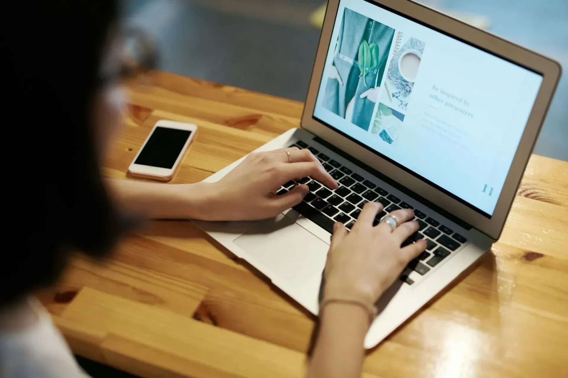 Person typing on a laptop at a wooden table with a smartphone beside it.