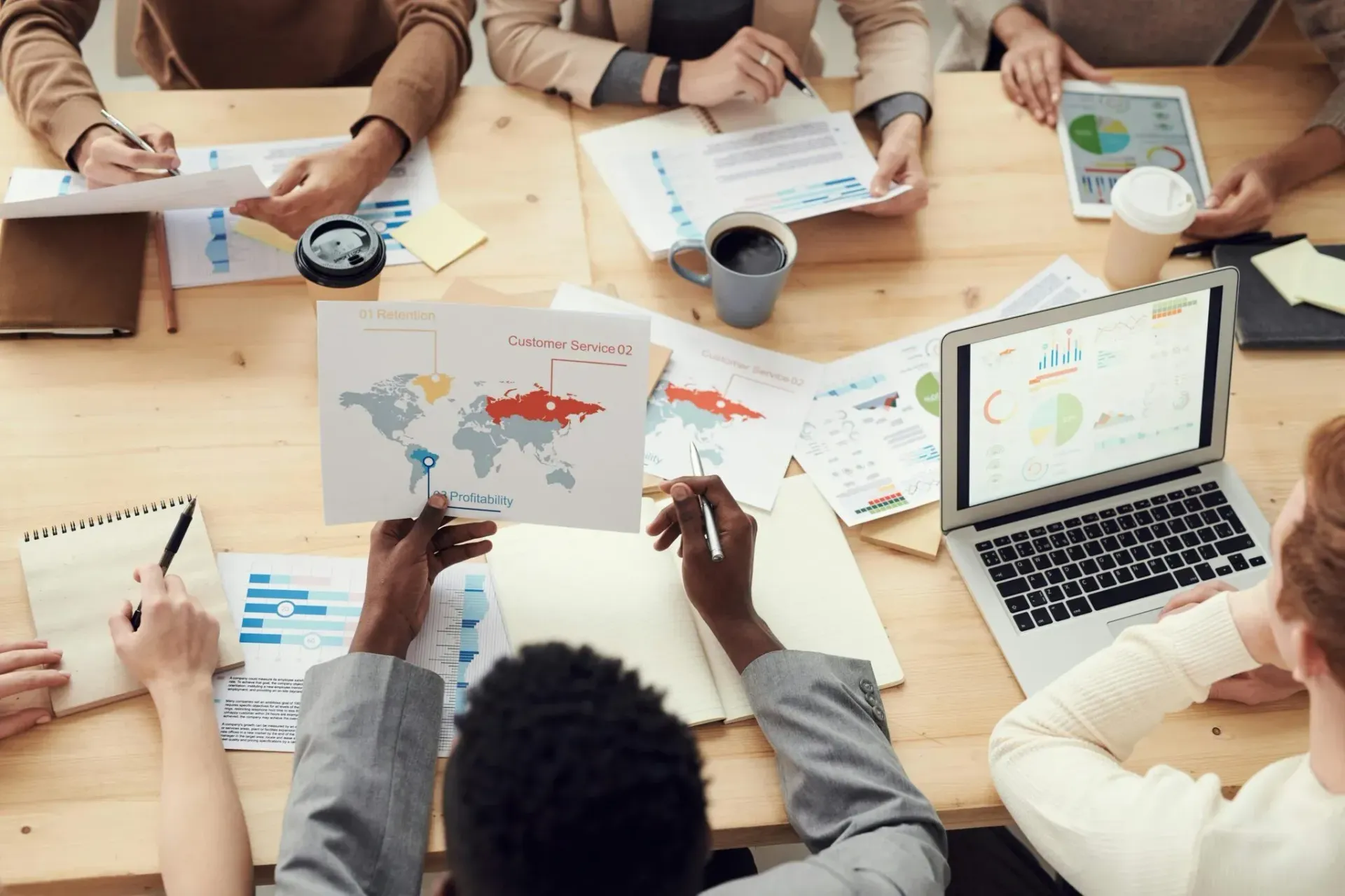 People collaborating around a table with maps, papers, and a laptop in a meeting room