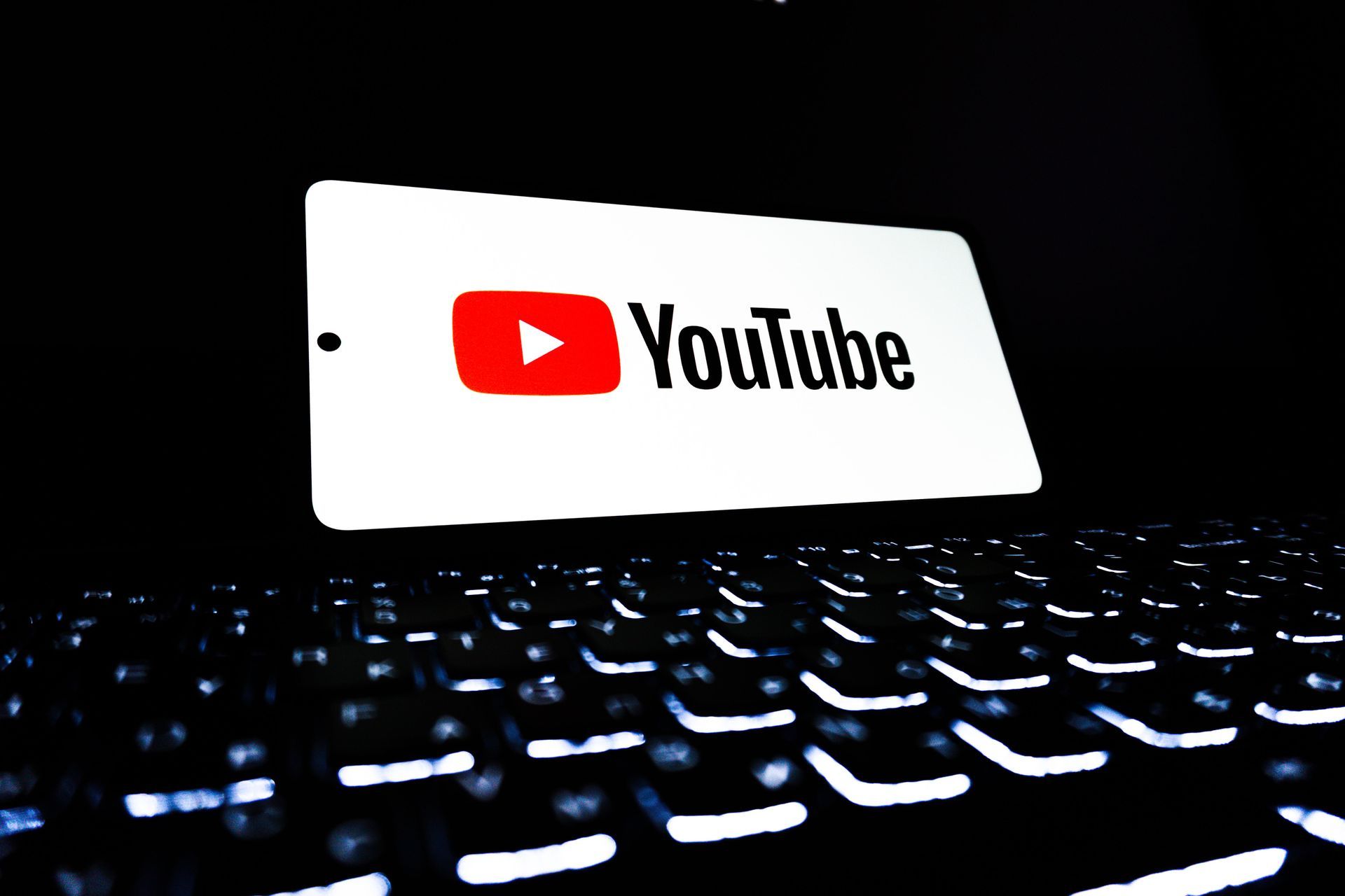 YouTube logo on a white card above a glowing keyboard in a dark setting