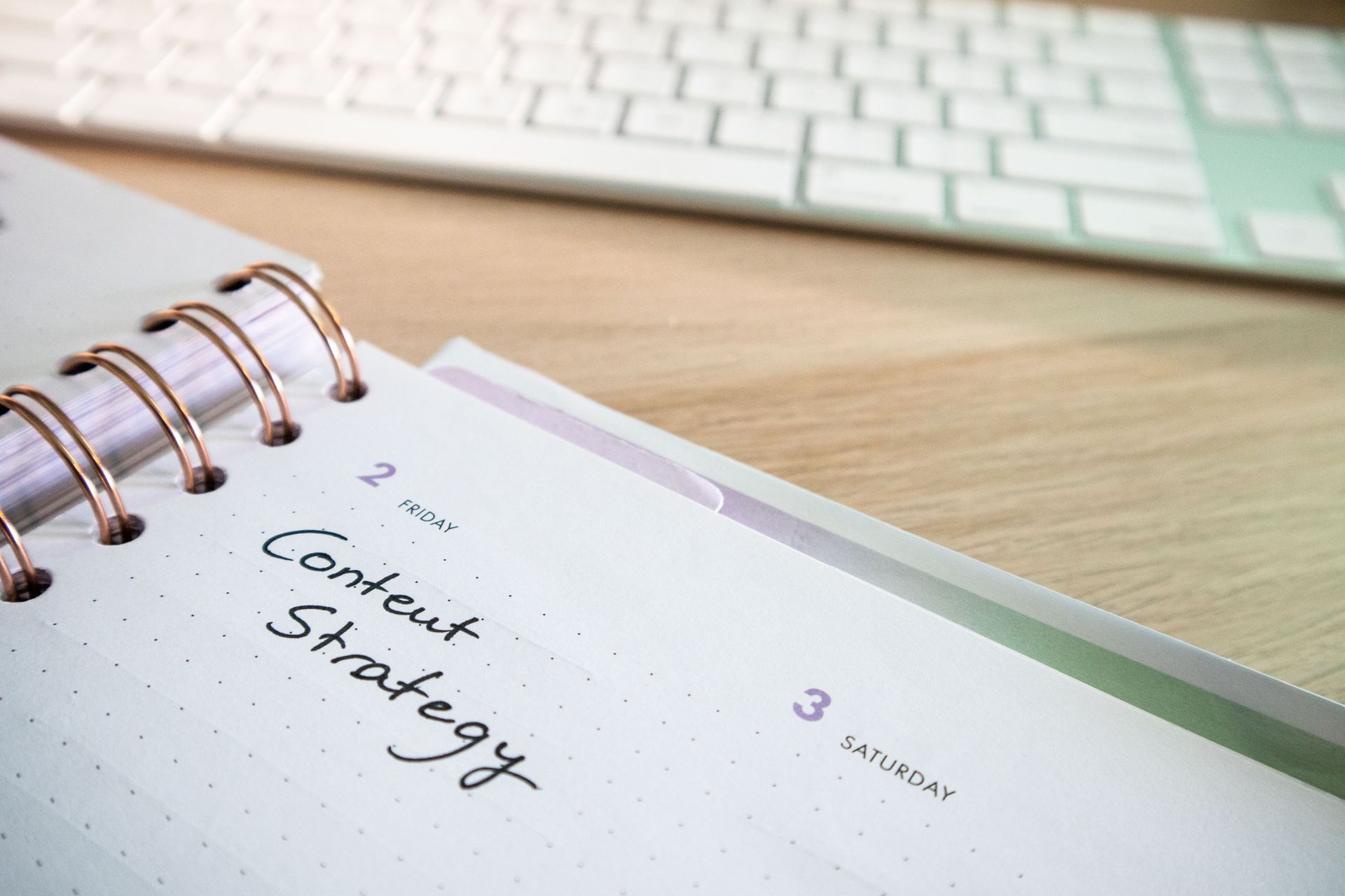 Notebook page with handwritten “Content Strategy” beside a white keyboard on a desk
