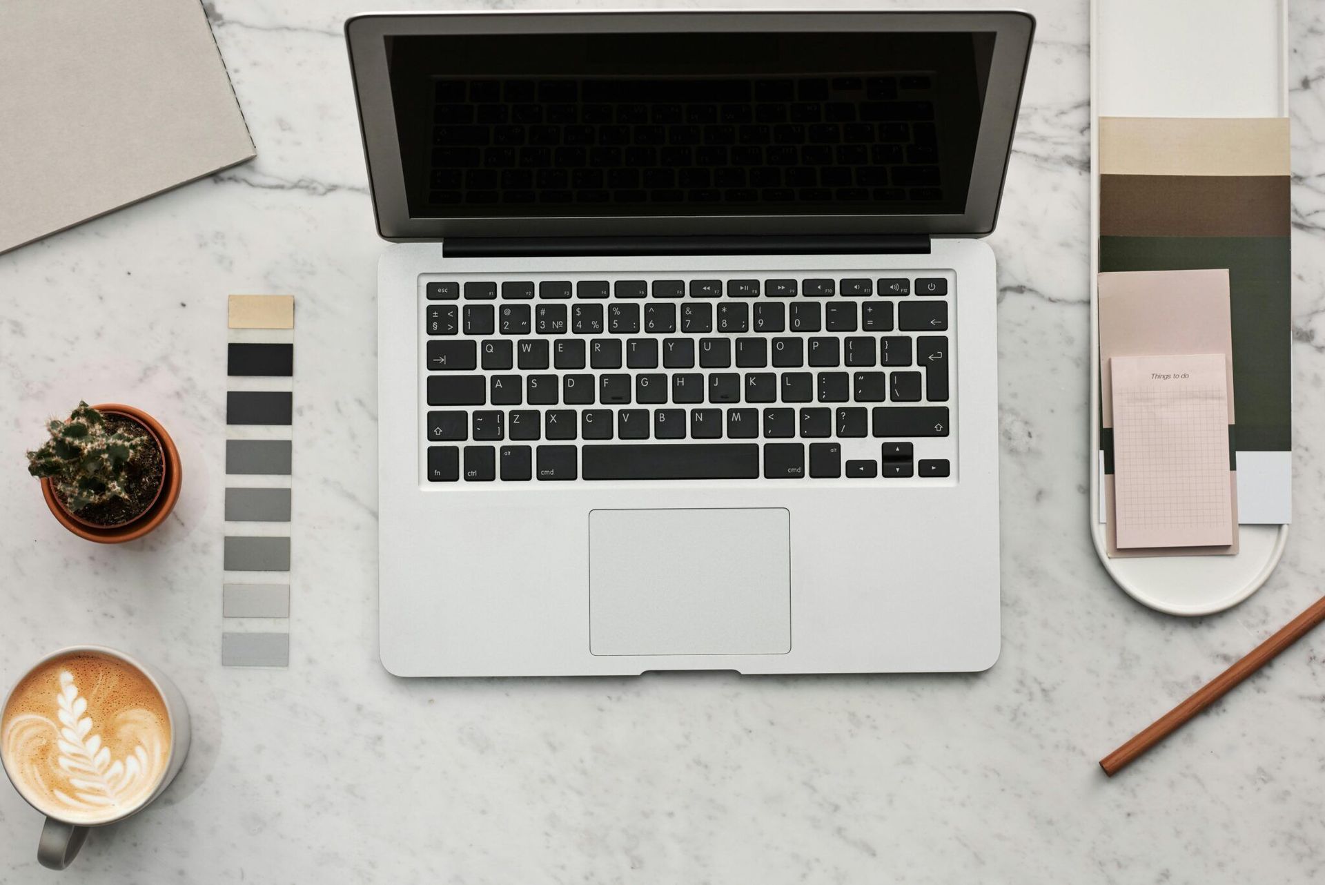 Top-down view of a laptop, coffee, color swatches, and notebook on a light desk.