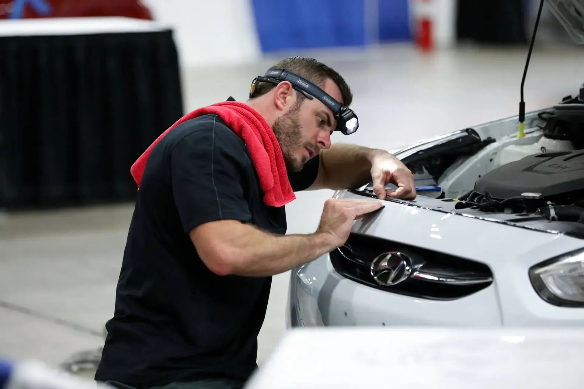 Mechanic inspecting a white car’s hood with a flashlight in a garage