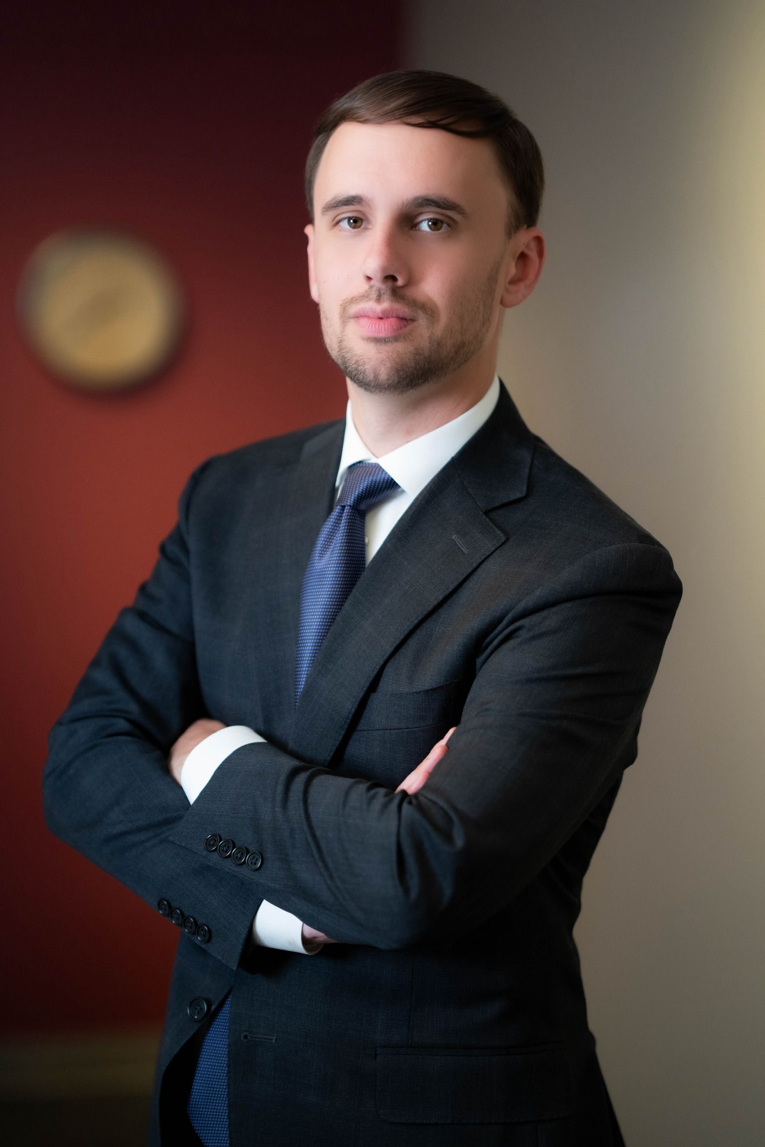 Man in a suit with arms crossed, looking directly at the viewer. Standing in an office setting.