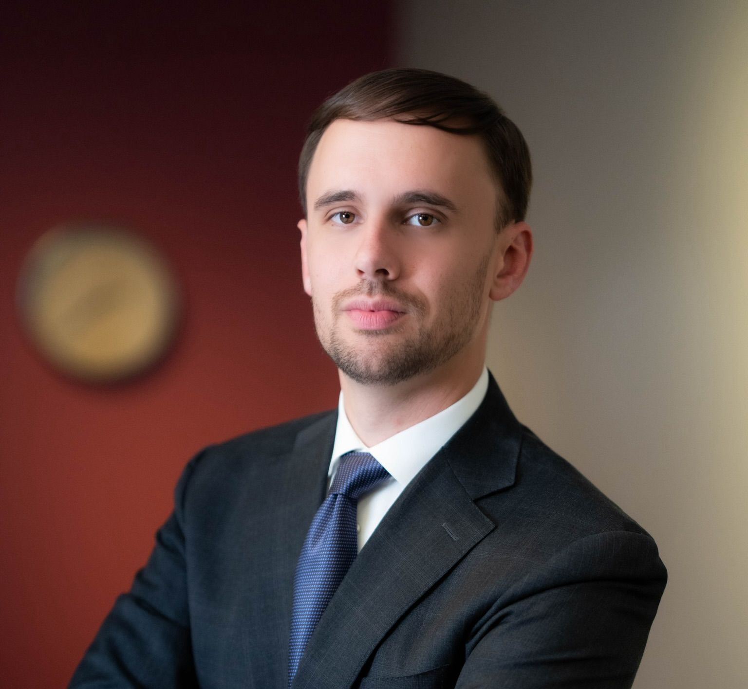 Man in a suit, looking directly at the viewer, indoors, red and beige background.