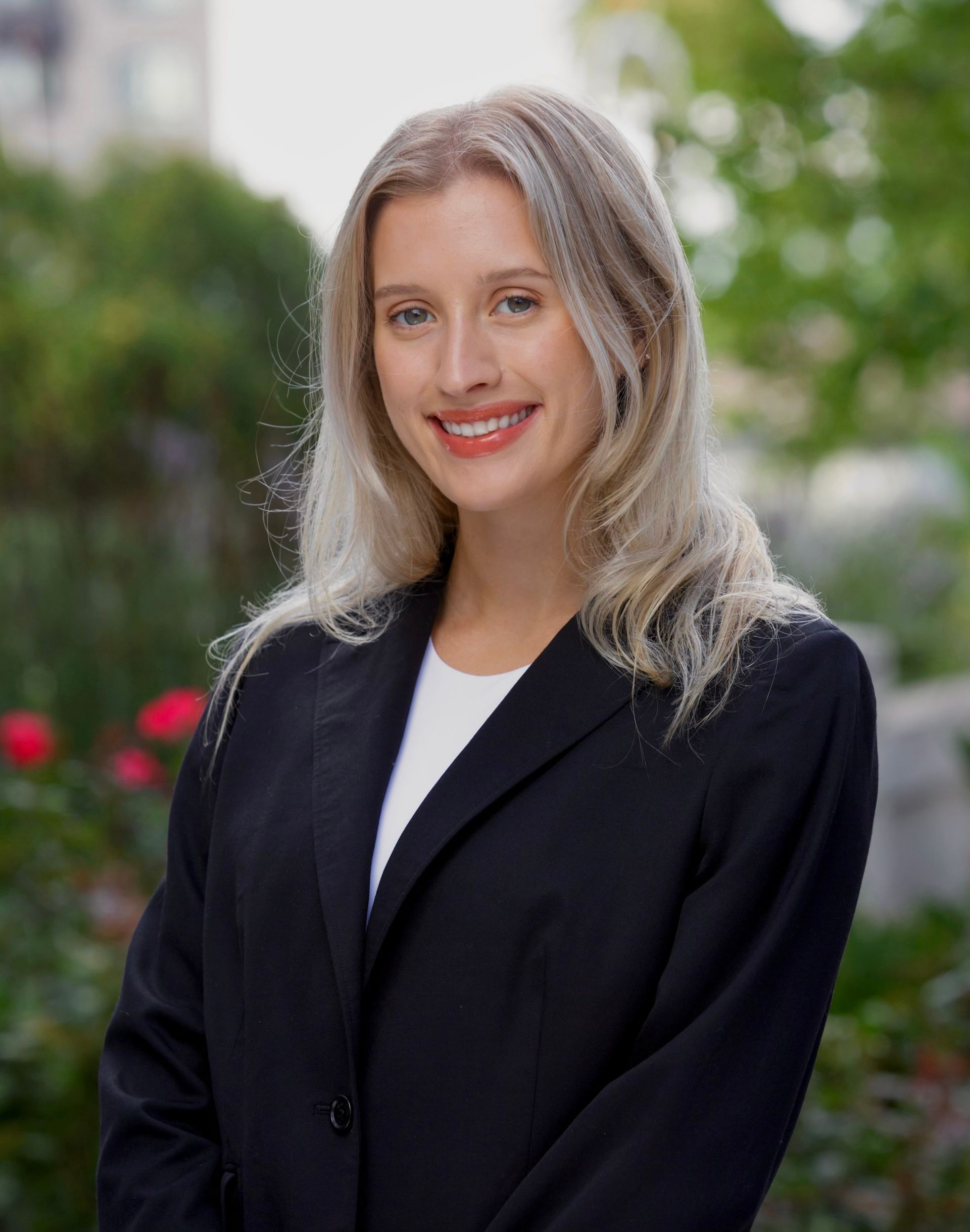 A woman in a suit and necklace is smiling for the camera.