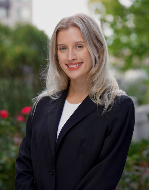 A woman in a suit and necklace is smiling for the camera.