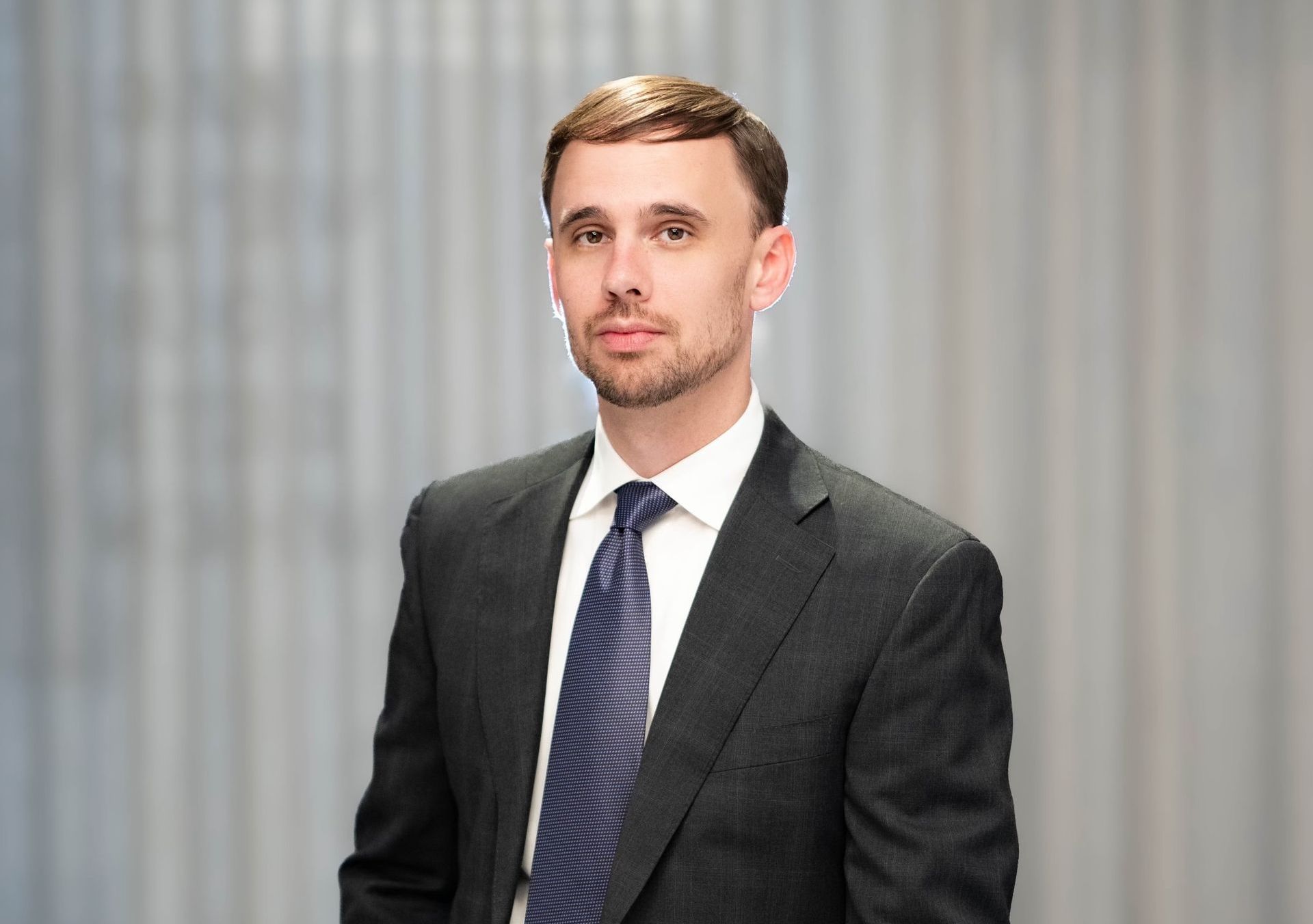 Man in suit and tie, looking at the camera in front of a blurred background.