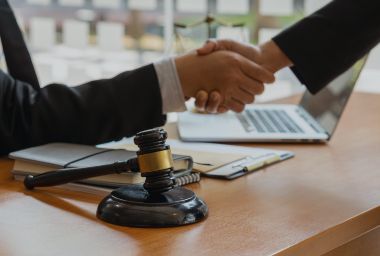 Two people shaking hands, gavel and laptop on table. Lawyers in office, sealing deal.