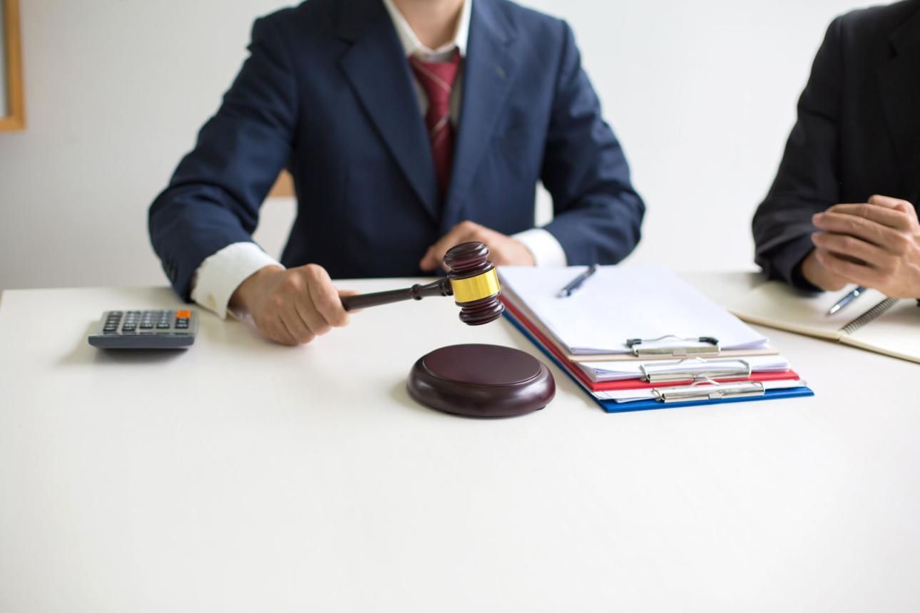 Judge’s gavel on desk beside files; two businesspeople seated in a meeting room