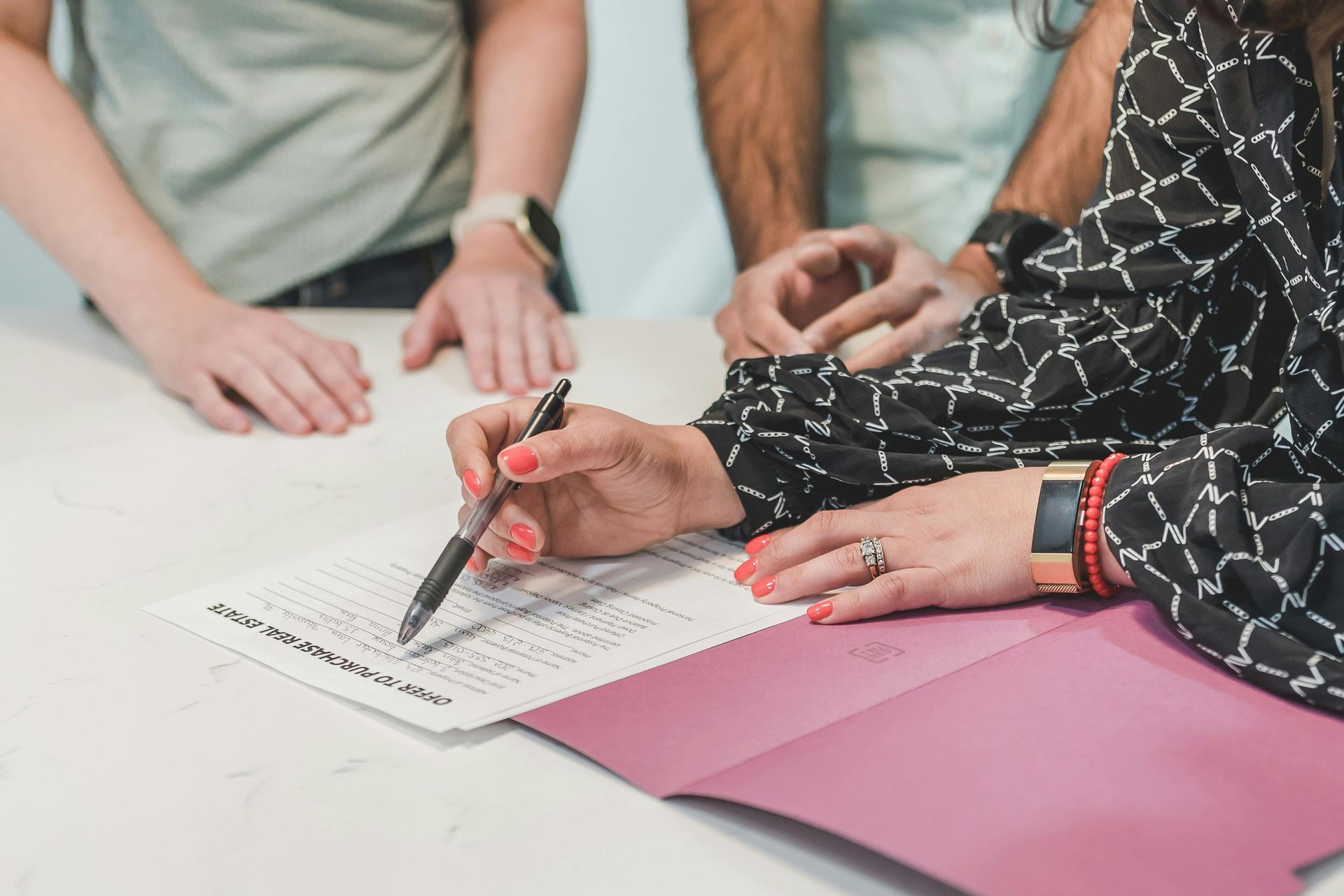 Woman signing document, two people standing behind, all at a table.