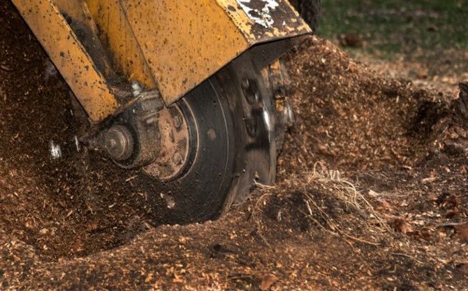 Yellow excavator bucket grinding through dirt, kicking up debris and dust.