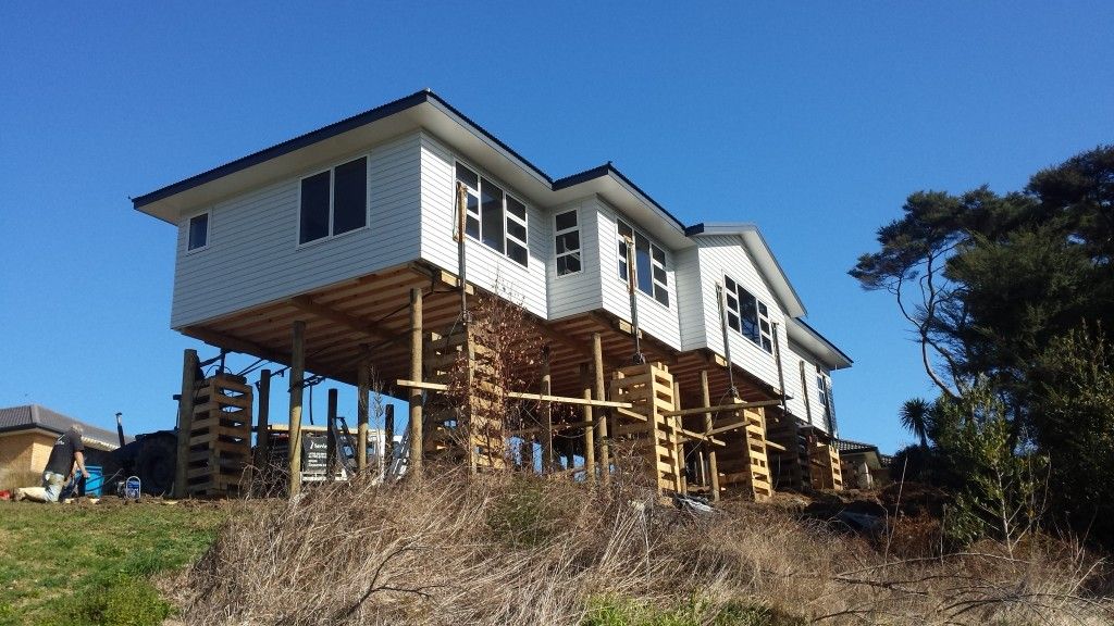 Raised house under construction on tall wooden stilts on a hillside under a blue sky