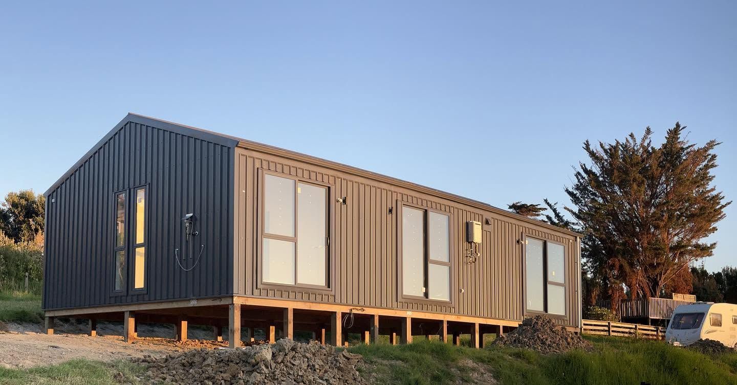 White house being installed on a trailer at a construction site, with a white porch and metal roof.