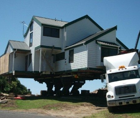 House being transported on a truck, lifted high off the ground on a clear day.