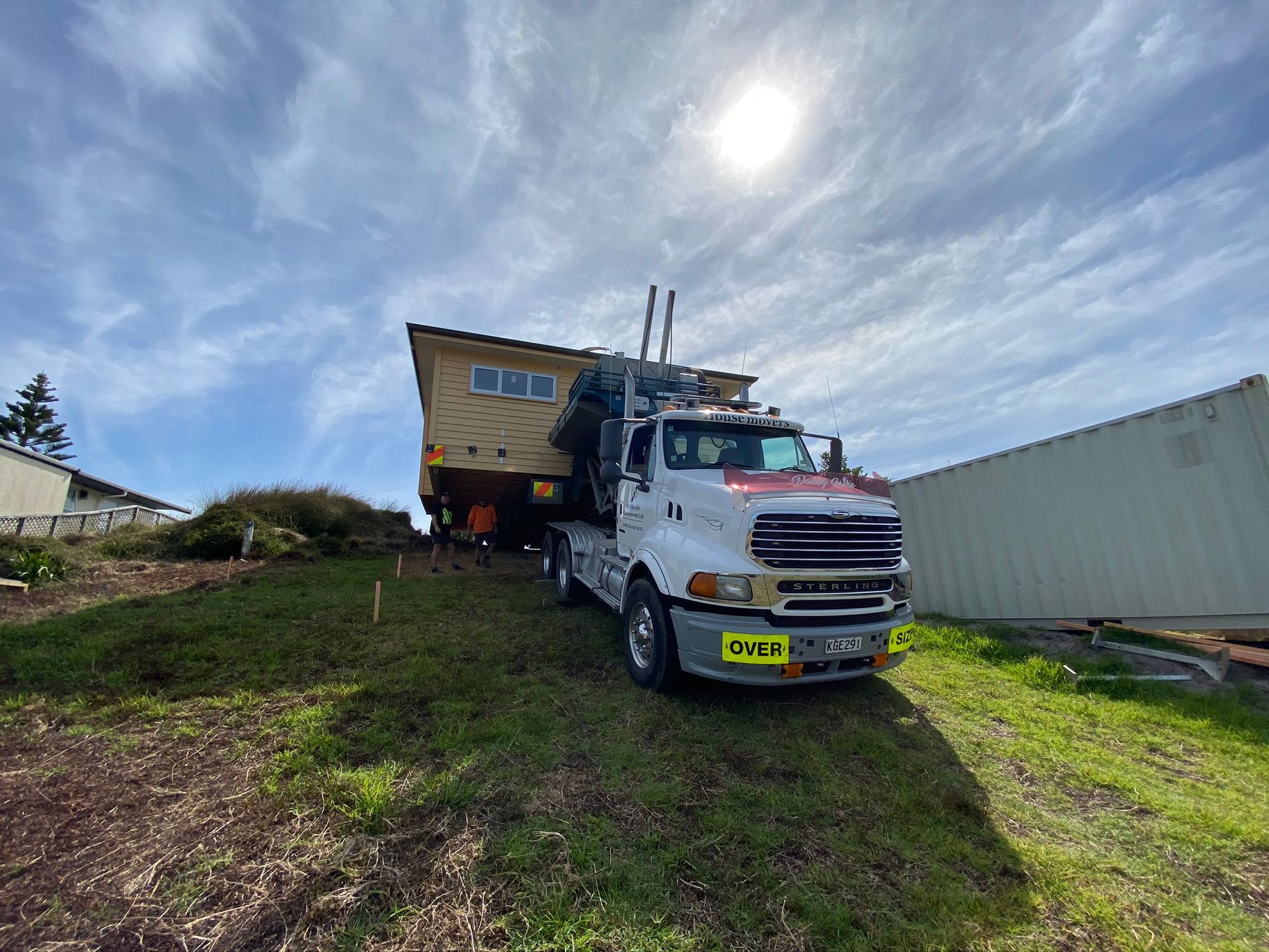 White truck with a large yellow trailer parked on a grassy slope under a cloudy sky.