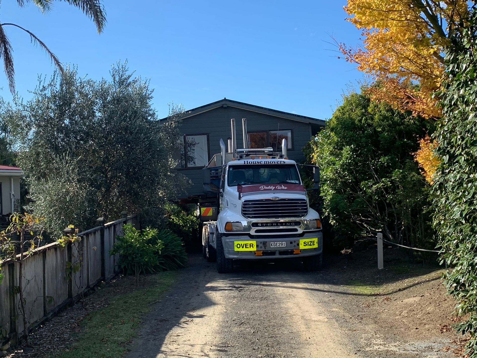 White truck parked on a gravel driveway in front of a house, framed by trees and a blue sky