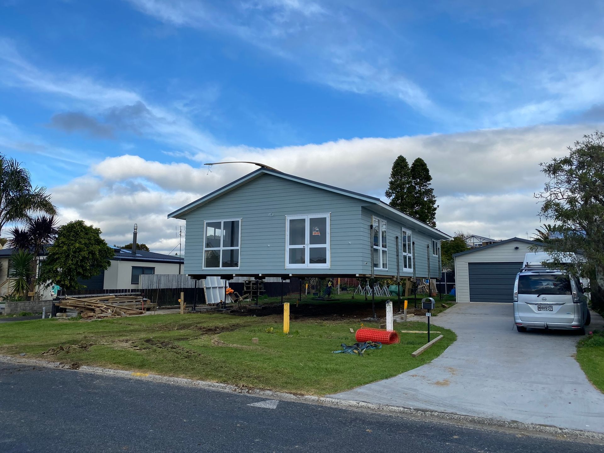 Gray house with white trim on a driveway under a partly cloudy blue sky