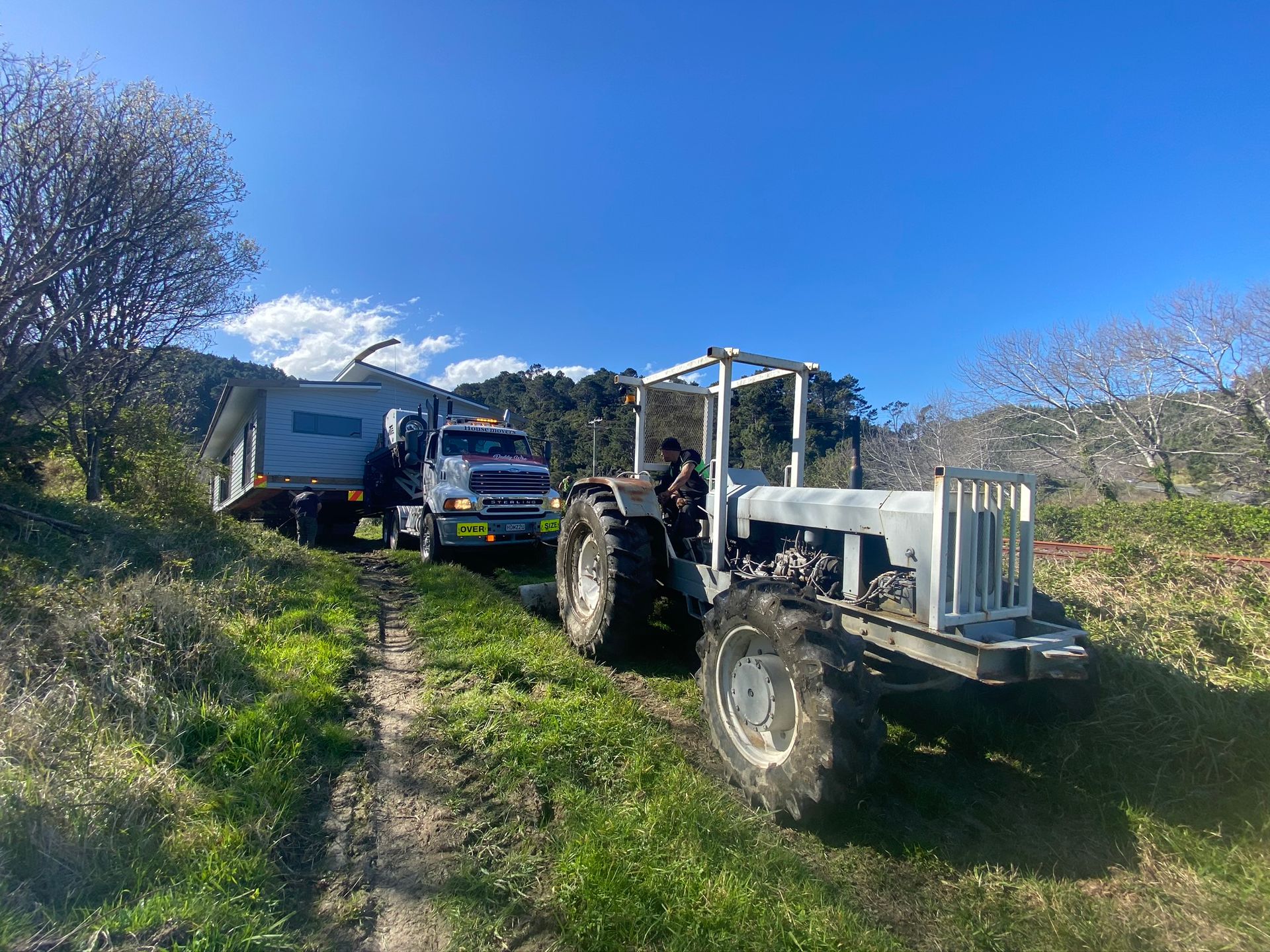 Two tractors parked on a grassy dirt path beside a blue truck under a clear blue sky.