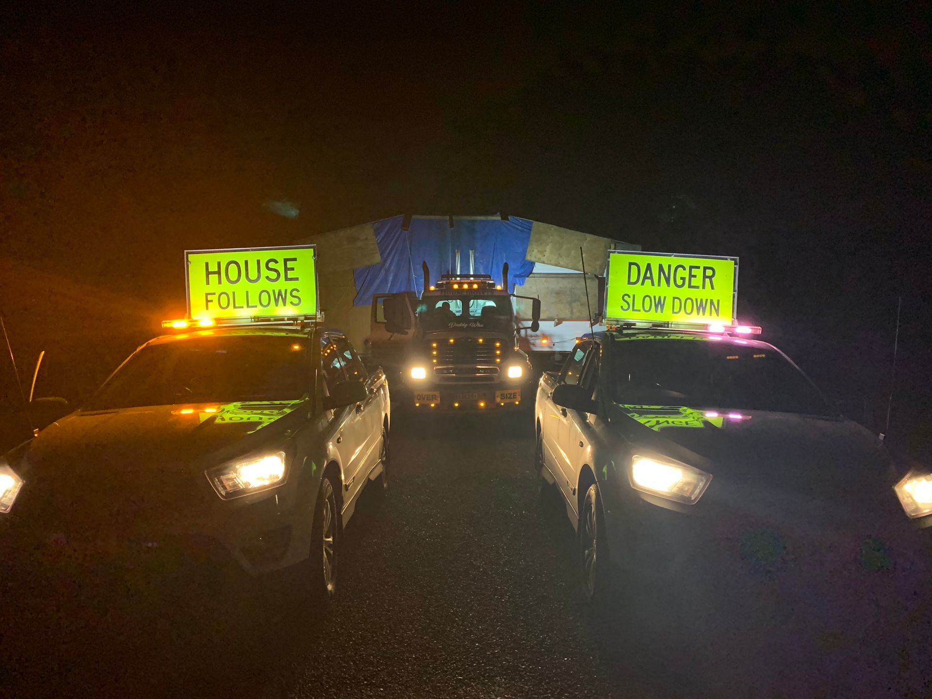 Night protest with cars and neon signs reading “HOUSE FOULS” and “DANGER: RISK OF RAIN” at night