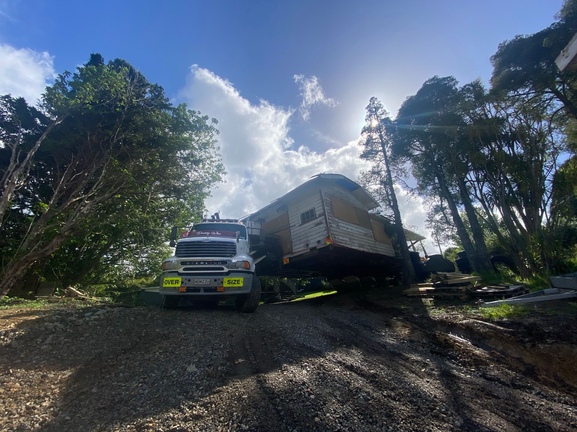 Truck and trailer on a gravel road in a wooded area, viewed from below under bright sky.