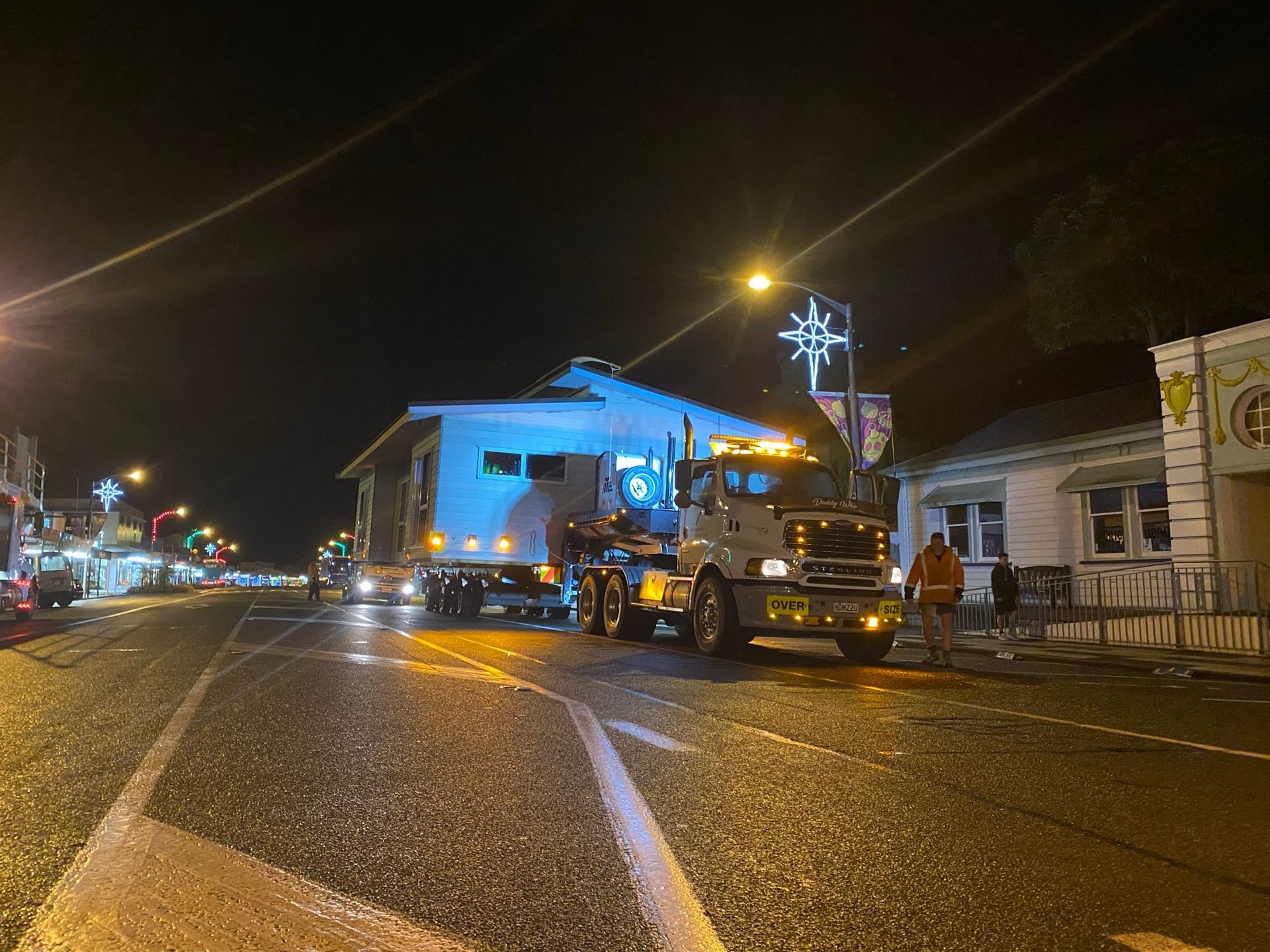 Night street scene with a blue-lit building and a tow truck on a wet road