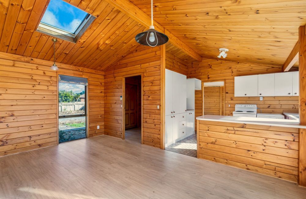 Wood-paneled kitchen and living area with skylight, white cabinets, and a door to the outside.