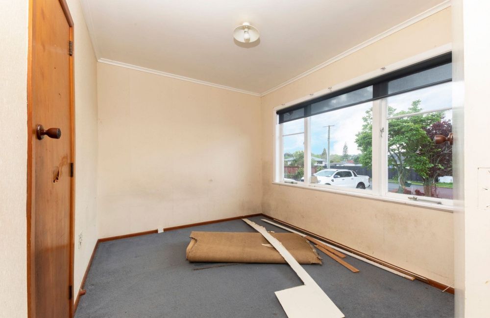 Empty room with beige walls, gray carpet, and large windows, with renovation materials on the floor