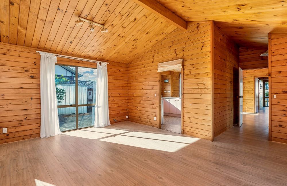 Empty wooden room with slanted ceiling, large windows, and sunlight on the floor