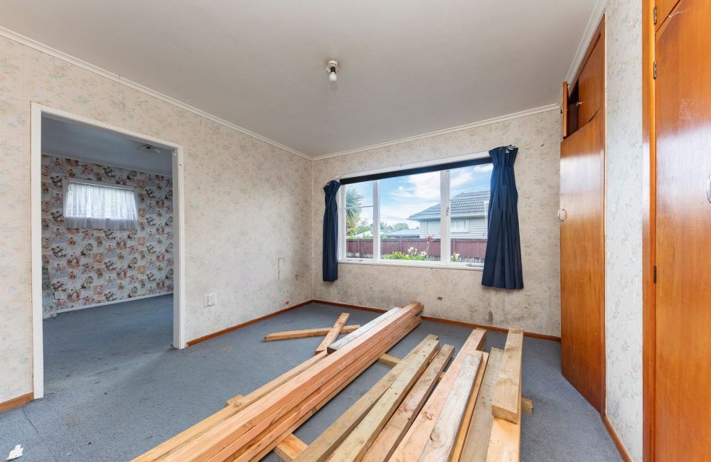 Empty bedroom with blue carpet, wooden closet doors, and stacked lumber on the floor near a window.