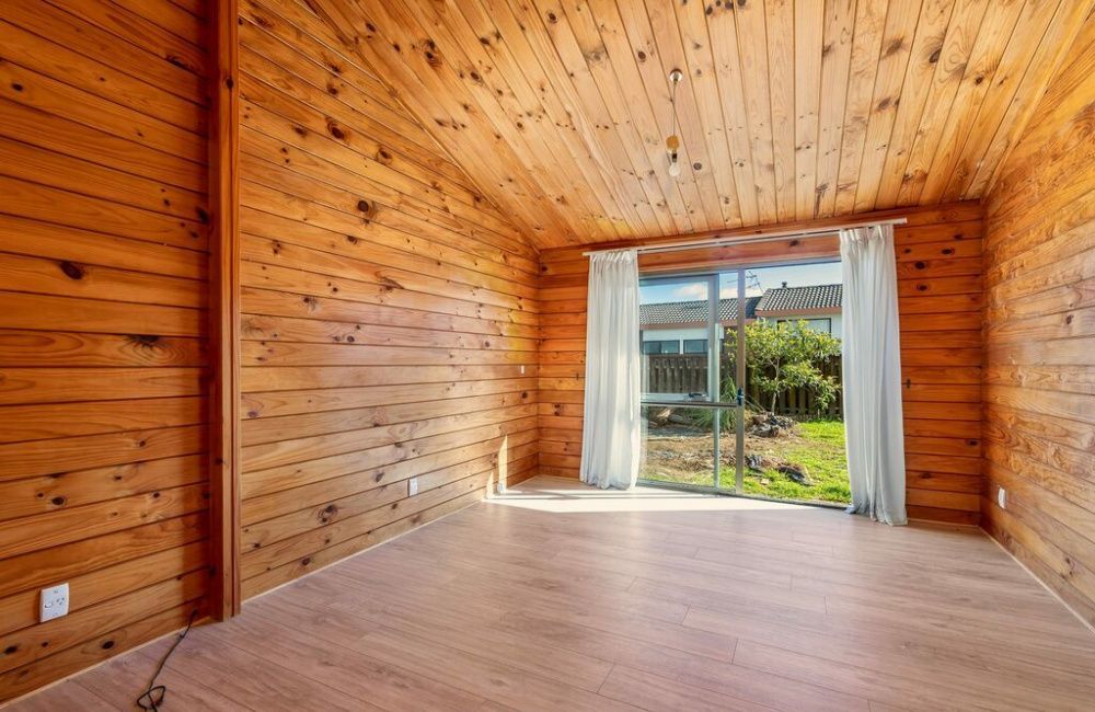 Empty wood-paneled room with a large window and sheer curtains overlooking a garden