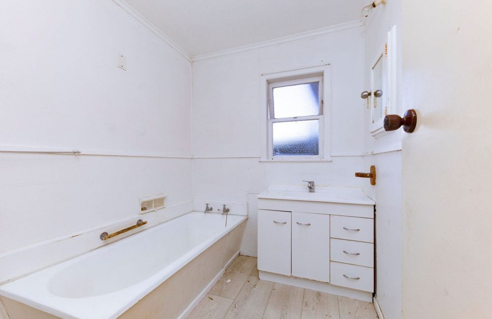 Bright white bathroom with a bathtub, sink cabinet, and small window