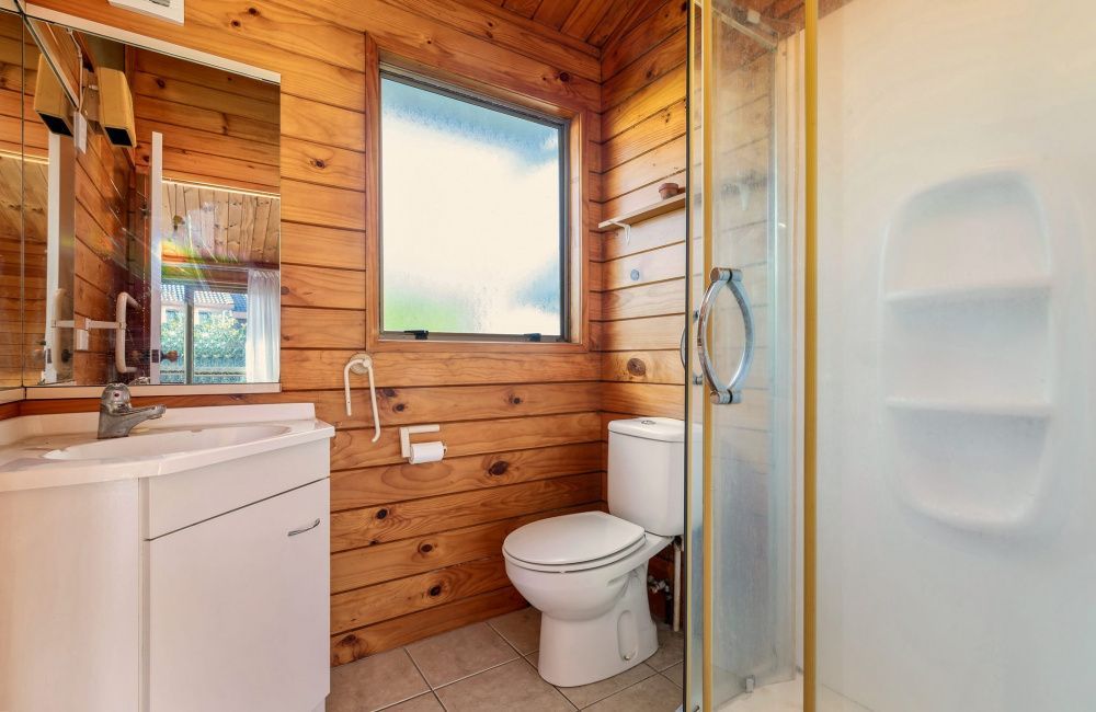 Small wood-paneled bathroom with a toilet, sink, shower, and window.