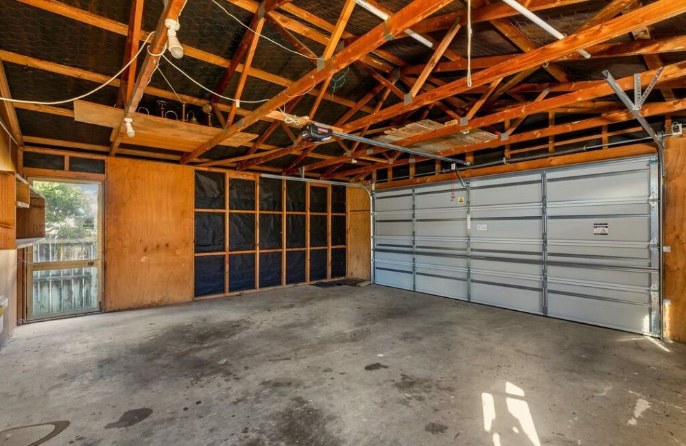 Empty garage interior with exposed wooden rafters, concrete floor, and a closed gray overhead door