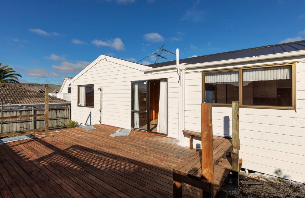 White house exterior with wooden deck and sliding glass doors under a blue sky