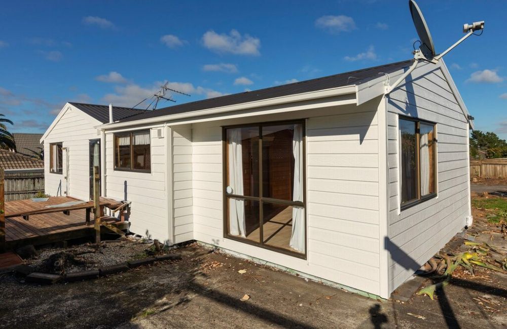 Small white house with sliding glass doors, a deck, and a satellite dish under a blue sky