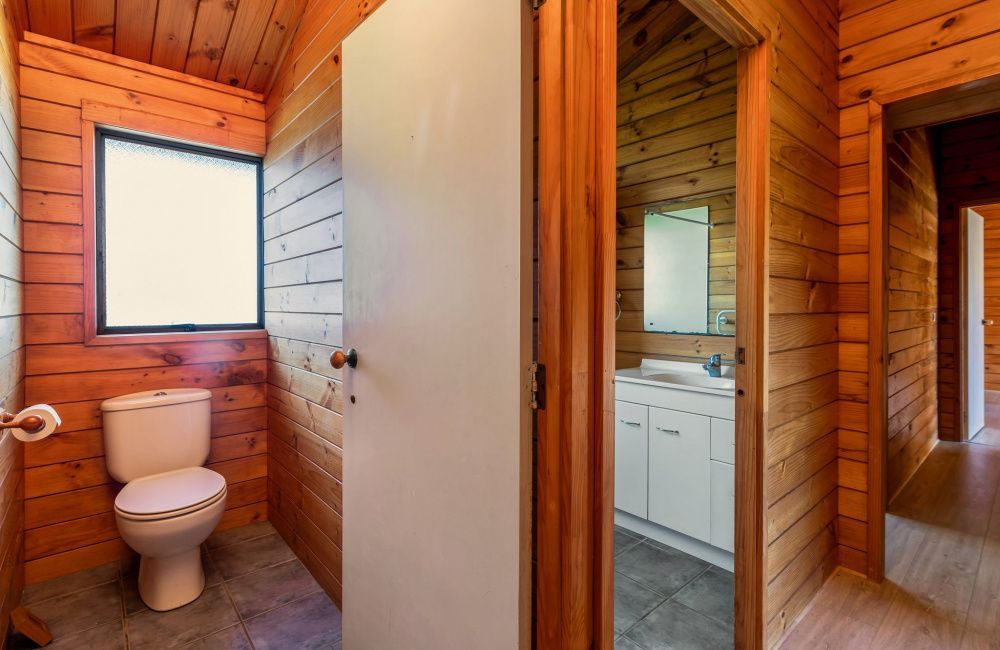 Rustic wood-paneled hallway with a bathroom, toilet, sink, and mirrored vanity visible through open doors.